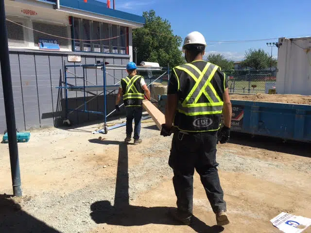 construction employees carrying a plank of wood